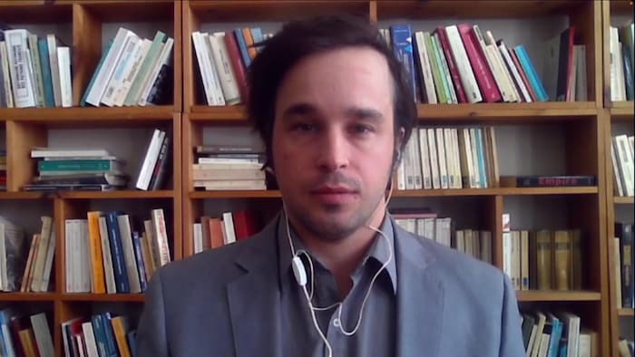 Colin Pratte during a video conference interview with a library full of books in the background.